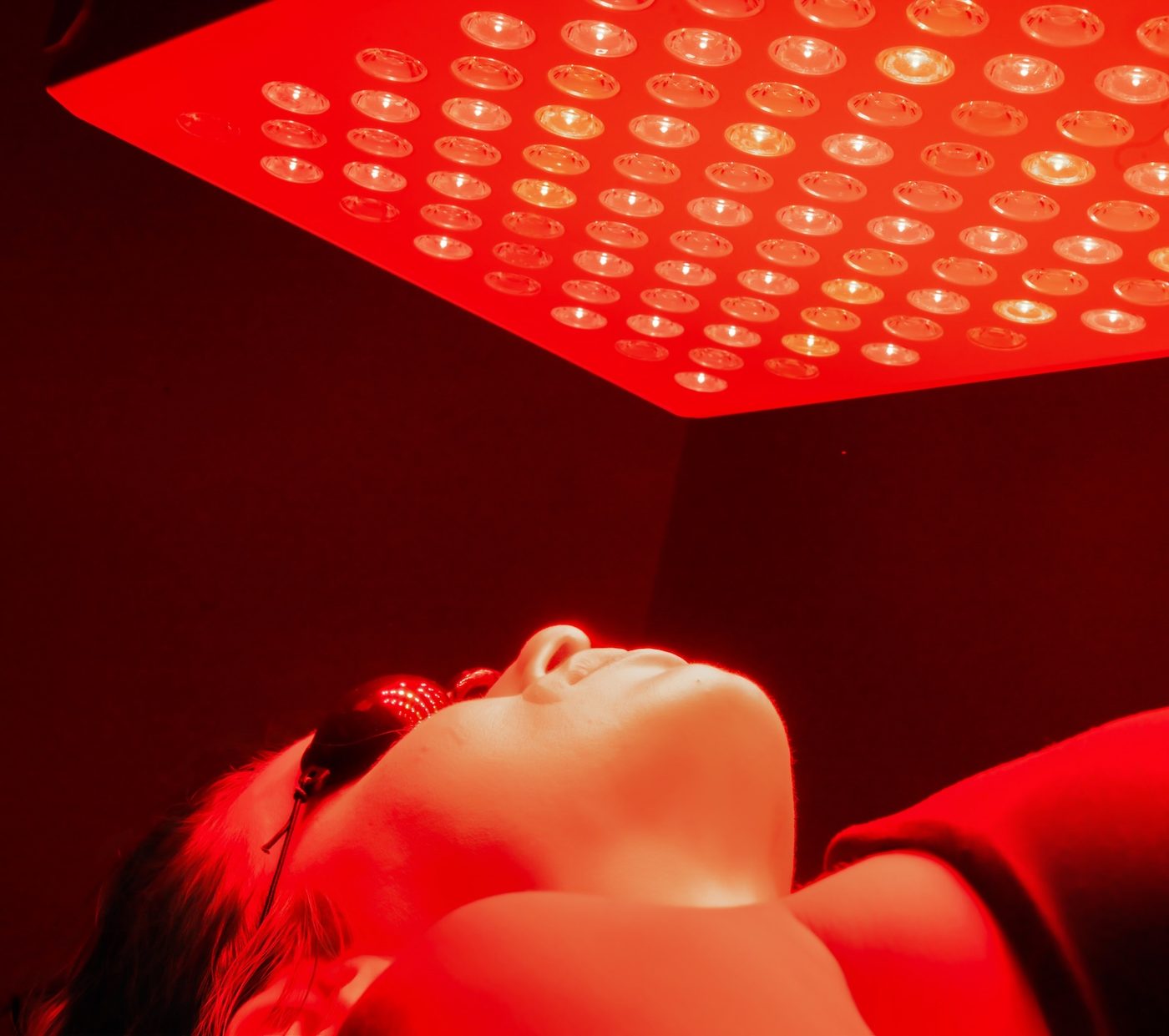A member under the medical-grade red light and near-infrared panel, wearing protective eyewear